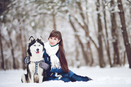 Girl sitting in the snow with a siberian husky dog in the winter forestの写真素材