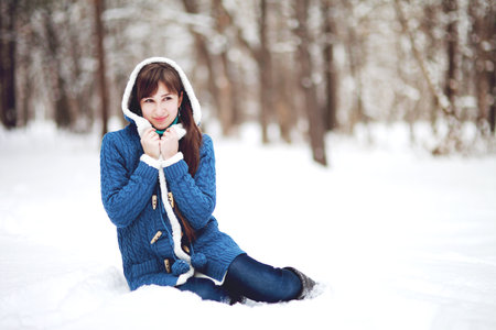 Winter portrait of a lovely girl in a blue sweater on the background of a snowy forestの写真素材