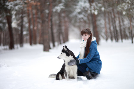Girl sitting in the snow with a siberian husky dog in the winter forestの写真素材