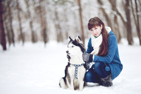Girl sitting in the snow with a siberian husky dog in the winter forestの写真素材