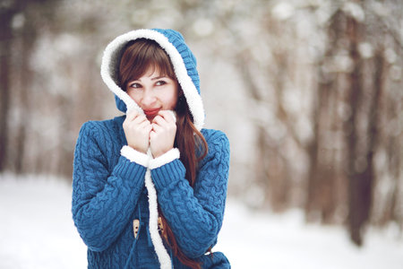 Winter portrait of a lovely girl in a blue sweater on the background of a snowy forestの写真素材