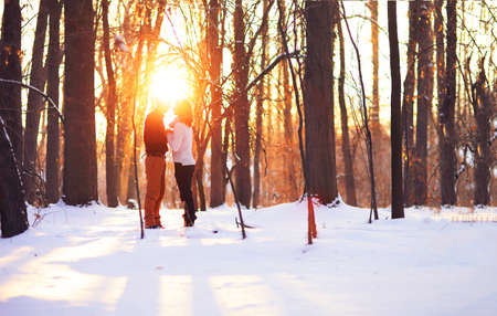 Young couple on winter holiday in a snowy forest at sunset.の写真素材