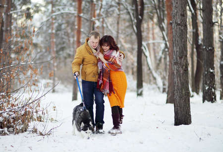 Young couple smiling and having fun in winter park with their husky dogの写真素材