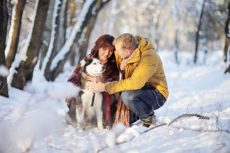 Couple smiling and having fun in winter park with their husky dogの写真素材