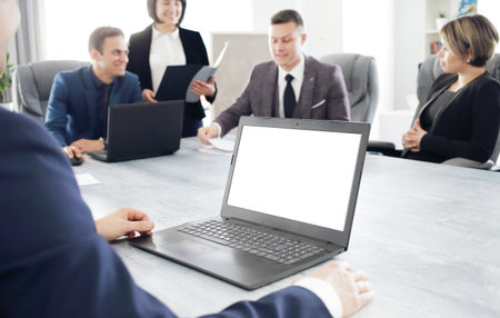 Laptop against the background of a group of young business people in the office discussing a work idea togetherの写真素材