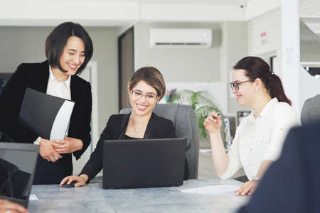 Three young successful business women in the office, together, happily working on a project.の写真素材