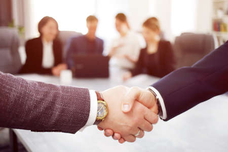 Business people shaking hands finishing a meeting in the background of their work team.の写真素材