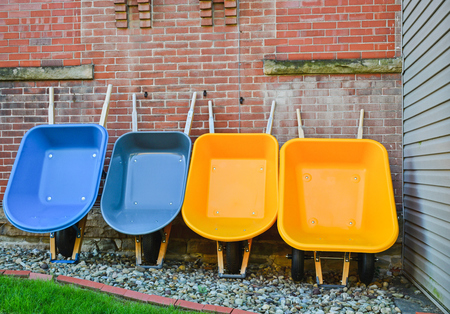 Four wheelbarrows, 2 yellow, 2 blue leaning against a wallの写真素材