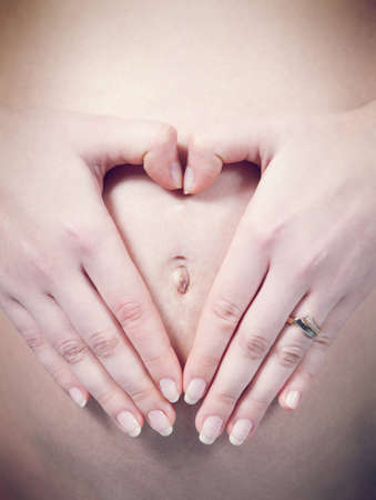Closeup fingers in heart shape over navel on pregnant white woman s belly  Pregnancy collection の写真素材