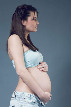 Beautiful pregnant white woman wearing light blue top and jeans  Long dark hair  Hands on belly  Pregnancy collection の写真素材