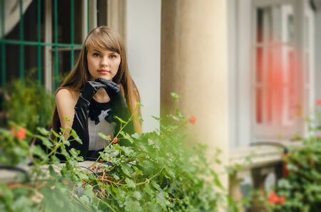 Portrait of beautiful young woman in white dress with black gloves standing at the porchの写真素材