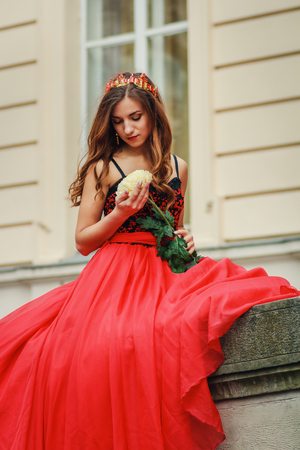 Beautiful young woman in red dress sitting at porch and holding the flowerの写真素材