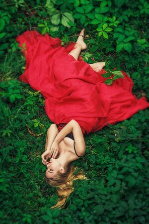 Beautiful young woman in fashion red dress lying in the green grapeの写真素材