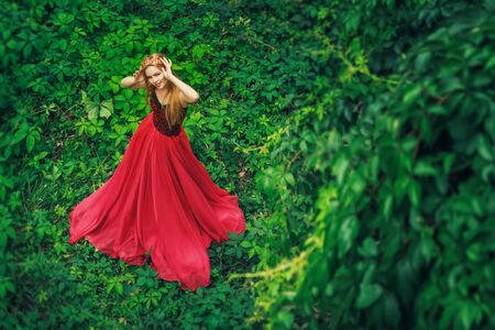 Beautiful young woman in fashion red dress standing in the green grapeの写真素材