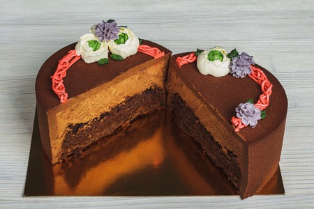 Chocolate cuted cake with cream flowers on light background