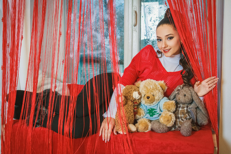 Beautiful young brunette girl with soft bear toys near the windowの写真素材