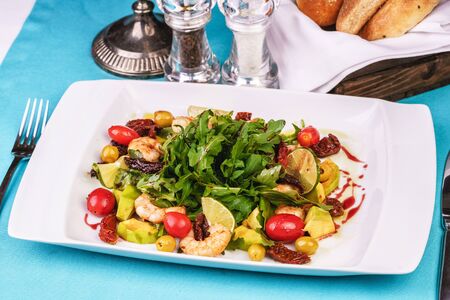 Grilled shrimps, cherry tomatoes, arugula, greens, avocado, lime and olives salad with balsamic dressingの写真素材