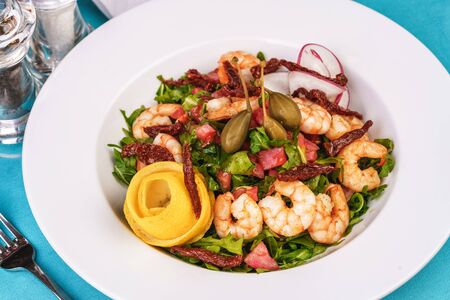 Mediterranean salad. Arugula, tomatoes, shrimps, olives, olives, basil and rosemary, dressed with olive oil and balsamic sauce, decorated with lemon and chili pepperの写真素材