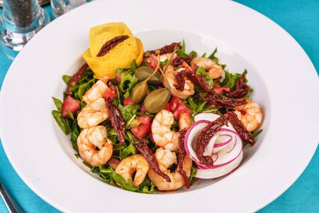 Mediterranean salad. Arugula, tomatoes, shrimps, olives, basil and rosemary, dressed with olive oil and balsamic sauce, decorated with lemon and chili pepperの写真素材