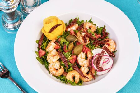 Mediterranean salad. Arugula, tomatoes, shrimps, olives, basil and rosemary, dressed with olive oil and balsamic sauce, decorated with lemon and chili pepperの写真素材