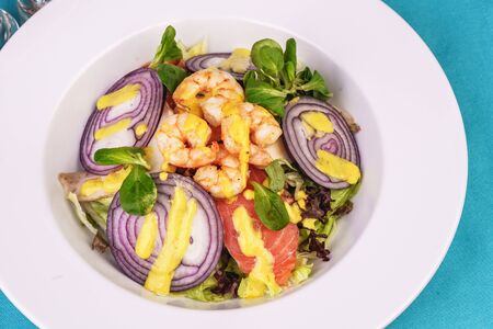 Mediterranean salad. Grilled prawns, smoked salmon, red onions and vegetables with dressing on topの写真素材