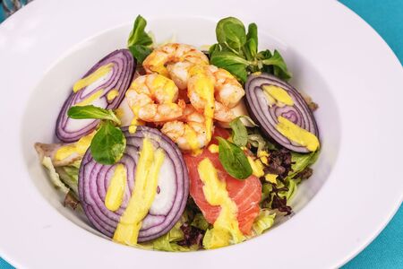 Mediterranean salad. Grilled prawns, smoked salmon, red onions and vegetables with dressing on topの写真素材
