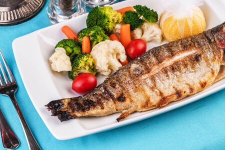 Mediterranean dish, European cuisine. whole fish baked in the oven, served with steamed vegetables - cauliflower, broccoli, carrots, cherry tomatoes and lemonの写真素材