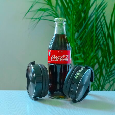Kazakhstan Almaty, October 18, 2019. A bottle of Coca-Cola with black headphones on a light...