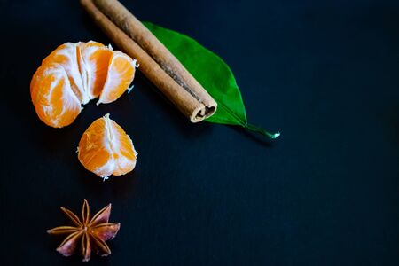 Dark textured christmas background with peeled tangerines, citrus leaves, star anise and cinnamon sticks. Background for banner, view from above.の写真素材