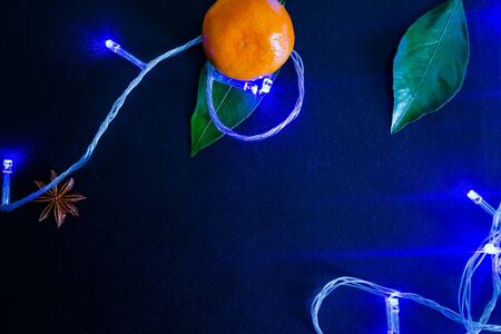 Dark textured christmas background with tangerines, citrus leaves, star anise, artificial star and cinnamon sticks and blue christmas garland. Background for banner. view from above.の写真素材
