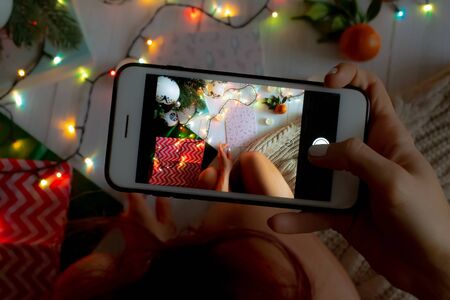 New Year concept, a girl takes a New Year's photo by the Christmas tree on the phone, a luminous garland, candles and gifts. Top view for new year or christmas banner. backgroundの写真素材