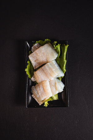 beautiful pike perch fillet on a green salad list on a black plate. View from above. Chinese...
