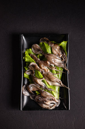 incredebly cooked octopuses with green salad on a black plate.Chinese cuisine, hotpot ingredient