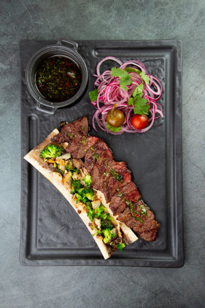 beef steak with sugar bone, served with sauce and salad of onions, pomilors and peppers. dark backgroundの写真素材