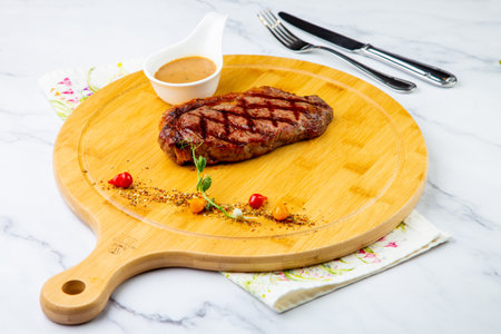 beef steak with spices and sauce on a wooden board on a marble backgroundの写真素材