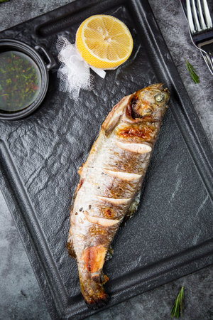 River trout baked in josper with sauce and lemon on a dark background top view