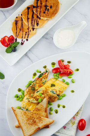 Breakfast of eggs and vegetables with cherry tomatoes and slices of bread in a white plate with pancakes top viewの写真素材
