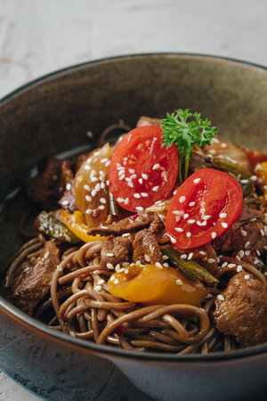 noodles with beef, vegetables, cherry tomatoes and sesame sauce in a deep plate side viewの写真素材