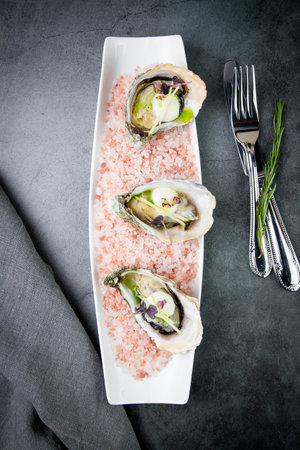 fresh oysters on red sea salt on a white plate top viewの写真素材