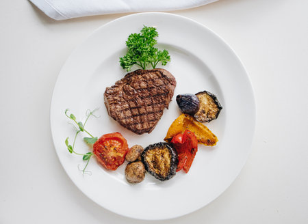 beef steak with grilled vegetables and herbs on a light background top viewの写真素材