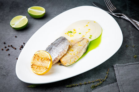 pieces of fried fish with sauce and fried lemon on a white plate side viewの写真素材