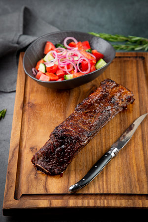 well-done steak with tomato and cucumber salad on a wooden tray, side viewの写真素材