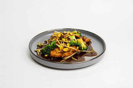 fried Asian dish with sweet and sour sauce, garlic and vegetables on a plate, side viewの写真素材