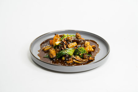 fried Asian dish with sweet and sour sauce, garlic and vegetables on a plate, side viewの写真素材