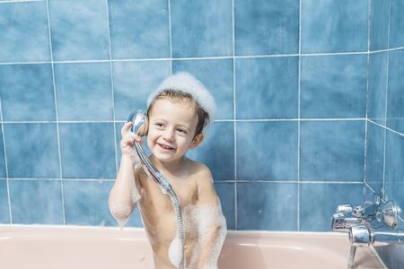 Color photography of a smiling child in the bathroom with his head full of foam and playing with the...