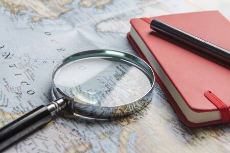 Photograph of a magnifying glass, a notebook and a pen on a world map.の写真素材