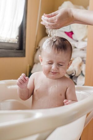 Color portrait of a baby in the bathroom pouring water over his head.