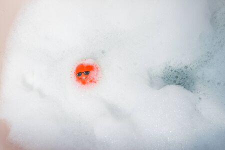 Color photograph of a red ball with a face drawn, floating in a foam bathの写真素材