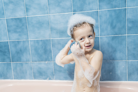 Color photography of a smiling child in the bathroom with his head full of foam and playing with the...