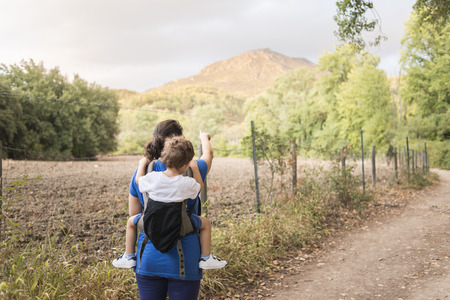 Color photograph of a mother with her son on her back hiking.の写真素材